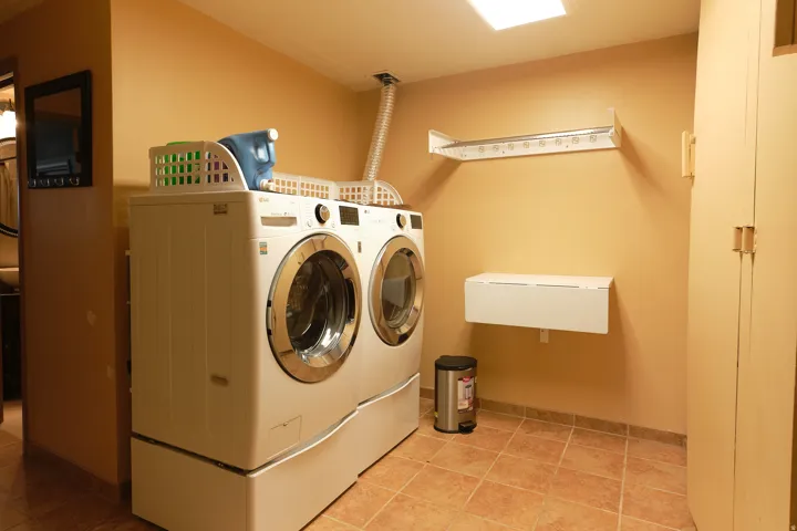 Laundry area with tile flooring, built-in cabinetry, wall-mounted folding shelf, and overhead drying rack