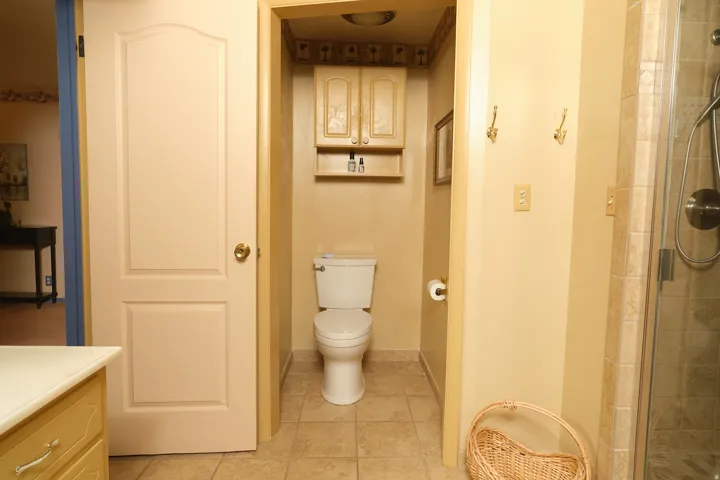 Recessed toilet area with built-in cabinetry and shelf, tile flooring, and a glass-enclosed shower