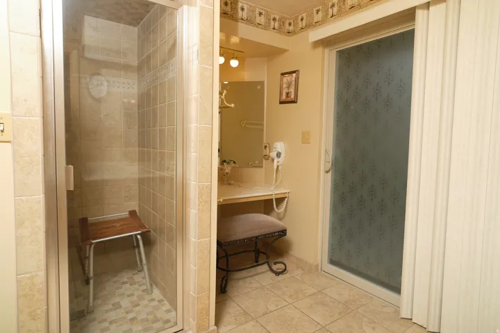 Tiled walk-in shower with glass enclosure, single vanity with integrated lighting, built-in countertop.
