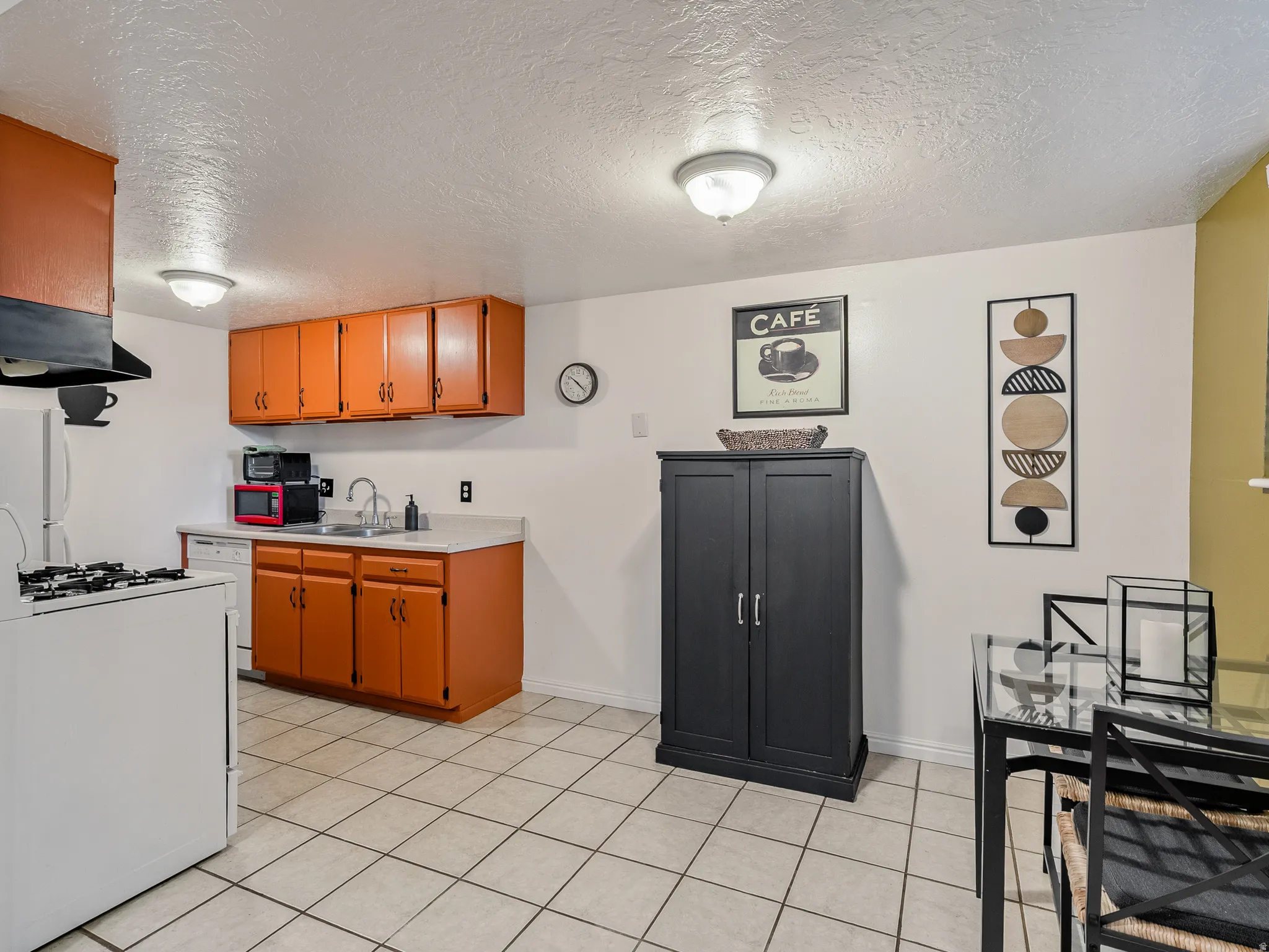 Kitchen featuring orange cabinetry, light countertops, a built-in dishwasher, a gas range, and square tiled flooring