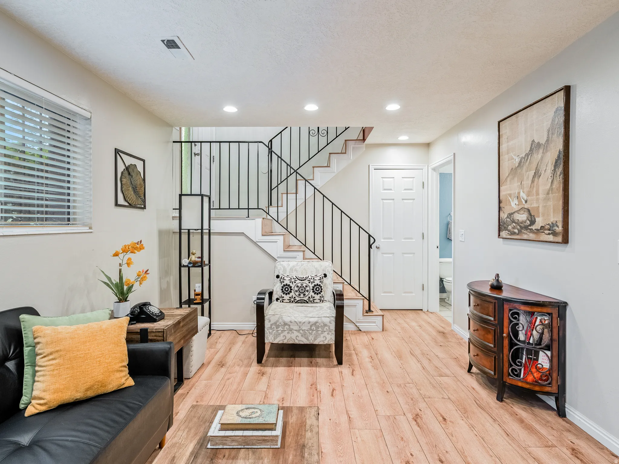 Wood-finish flooring, recessed ceiling lighting, stairway with dark metal railing, paneled interior door, and window with blinds