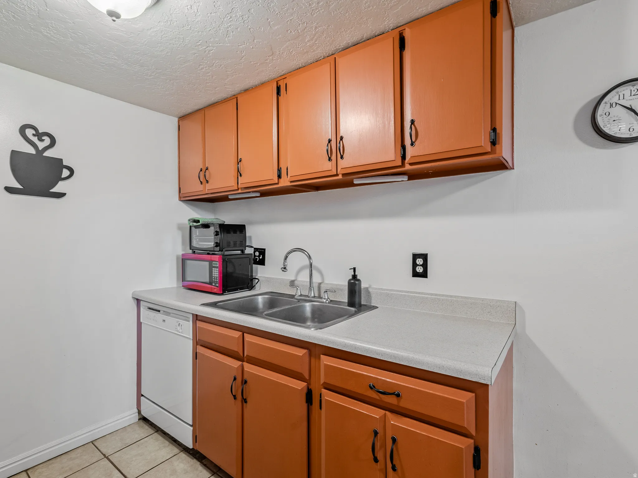 Kitchen featuring wood-finish cabinetry, light-toned countertops, and a double basin stainless steel sink