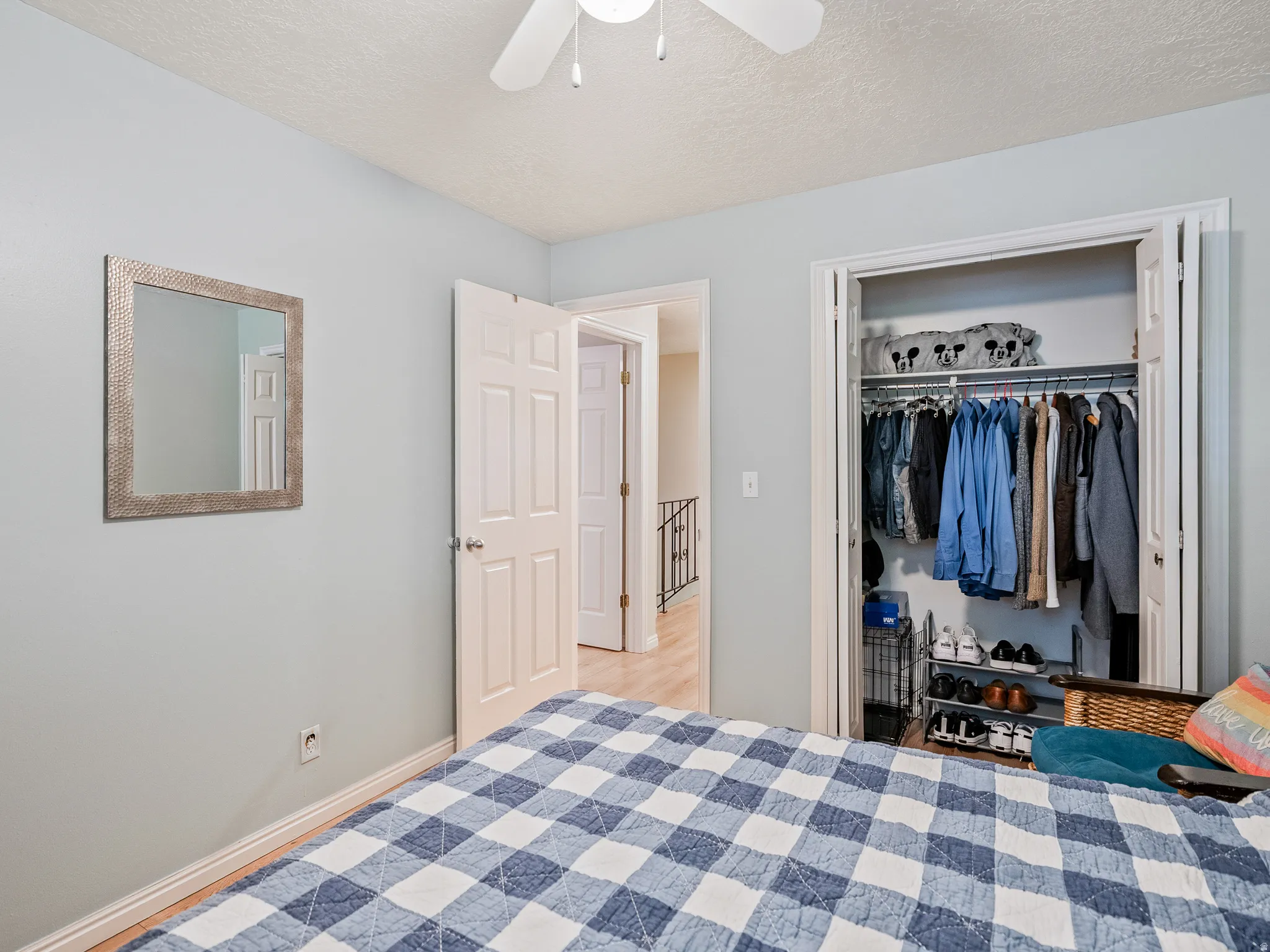 Light-colored walls with trim, wood-finish flooring, a built-in closet with bi-fold doors, and a ceiling fan