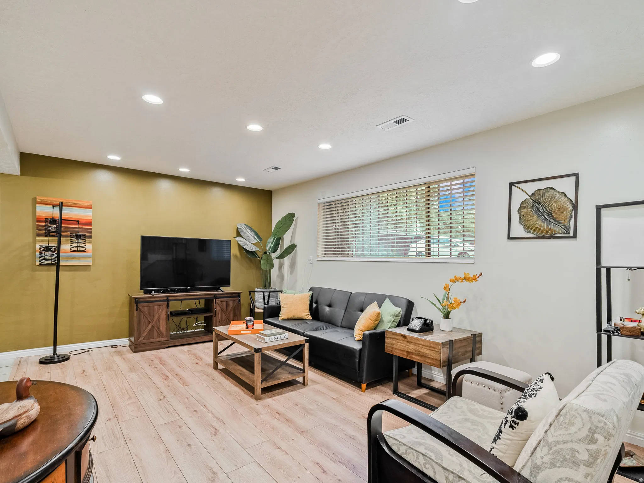 Recessed lighting illuminates the wood-finish flooring and a window with horizontal blinds