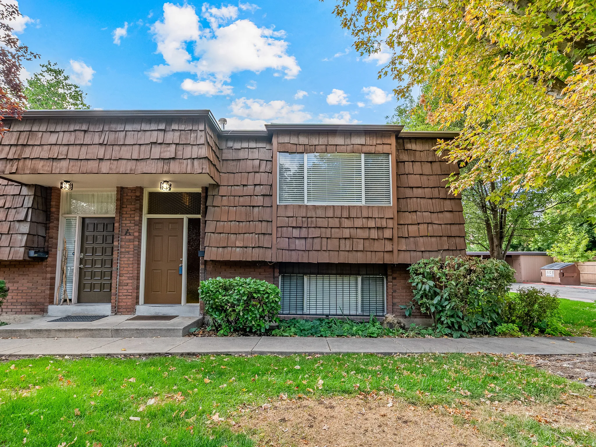 Cedar shake siding, brick facade, mature landscaping, front entry, lower-level window