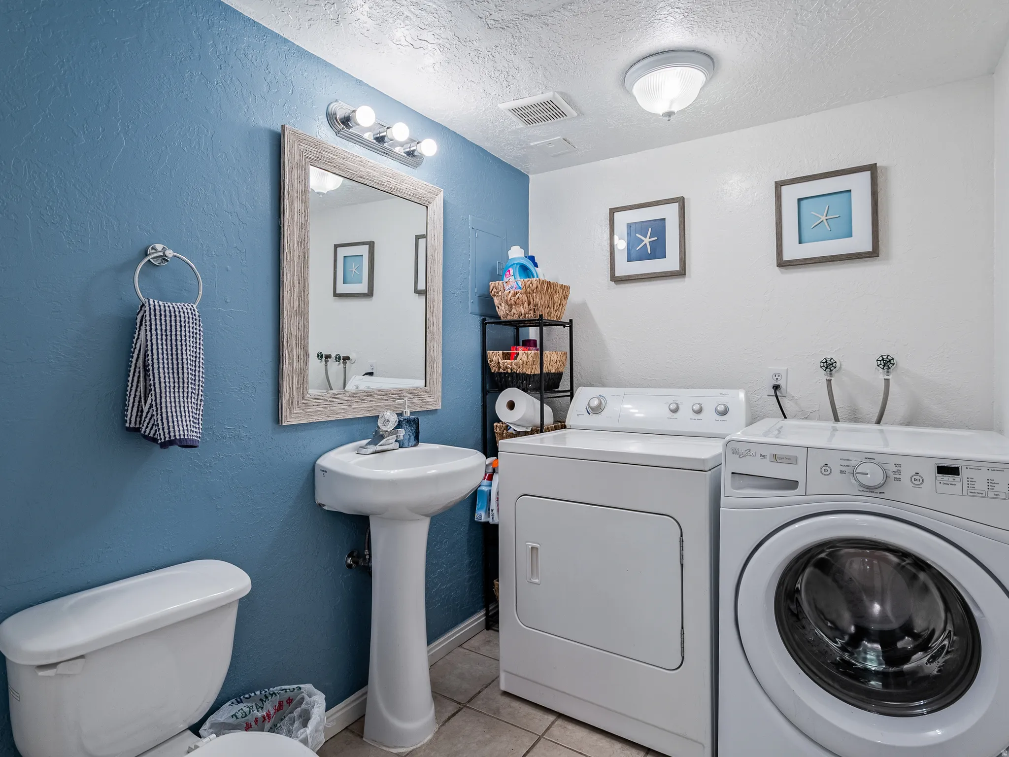 Pedestal sink with a framed mirror, attached vanity lighting, and ceramic tile flooring