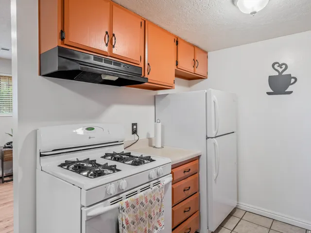 Kitchen featuring overhead cabinetry, a gas range, a white refrigerator, a light-colored countertop, and tiled flooring