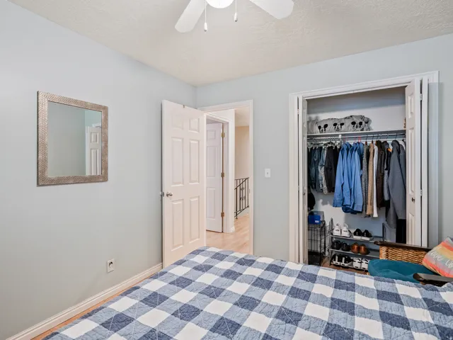Light-colored walls with trim, wood-finish flooring, a built-in closet with bi-fold doors, and a ceiling fan