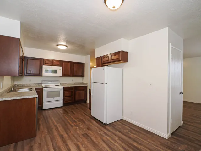 Kitchen featuring wood-finish flooring, dark wood cabinetry, white appliances, and light-toned countertops