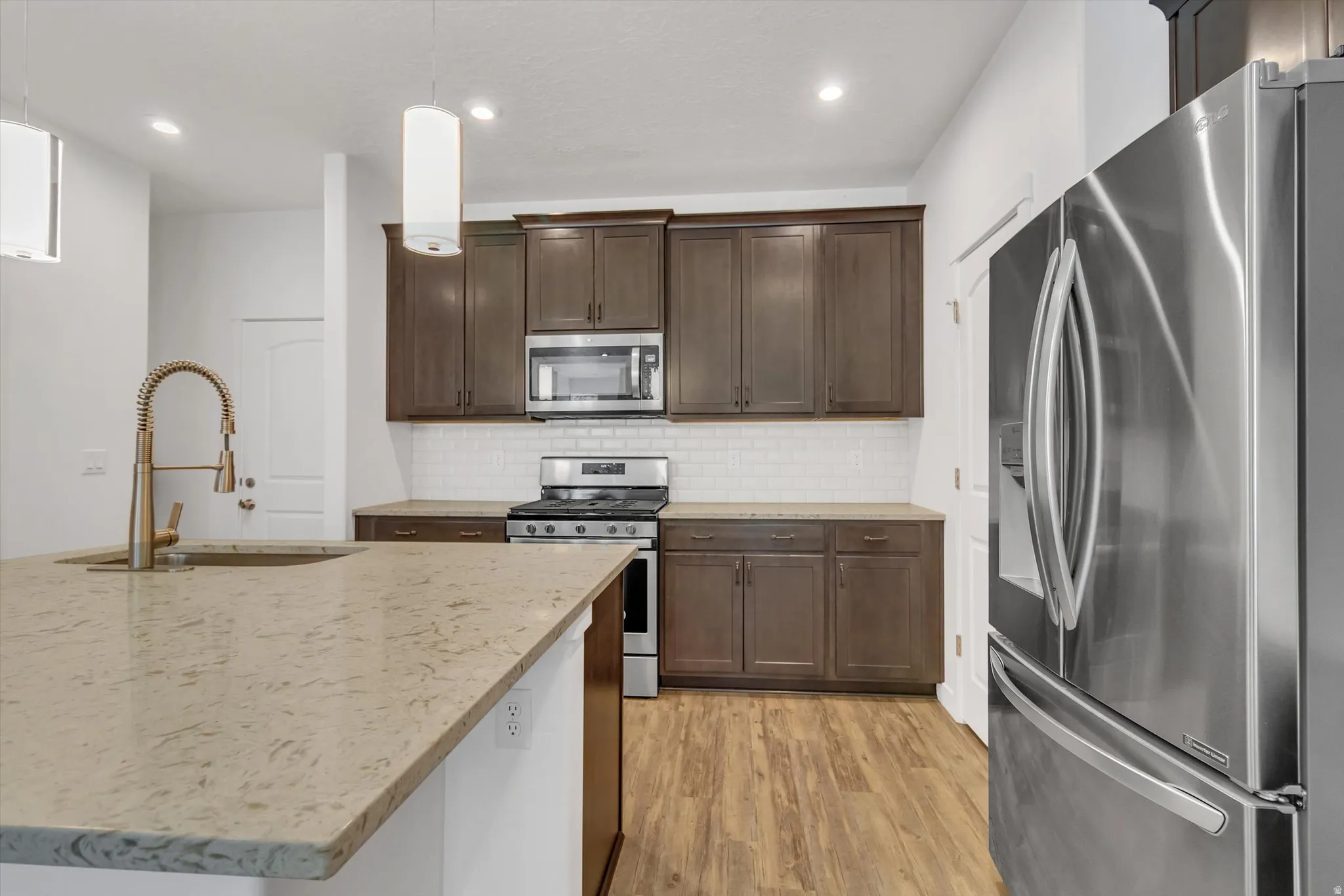 Kitchen featuring a large island with stone countertop, stainless steel appliances, dark wood-finish cabinetry, white subway tile backsplash, and wood-finish flooring