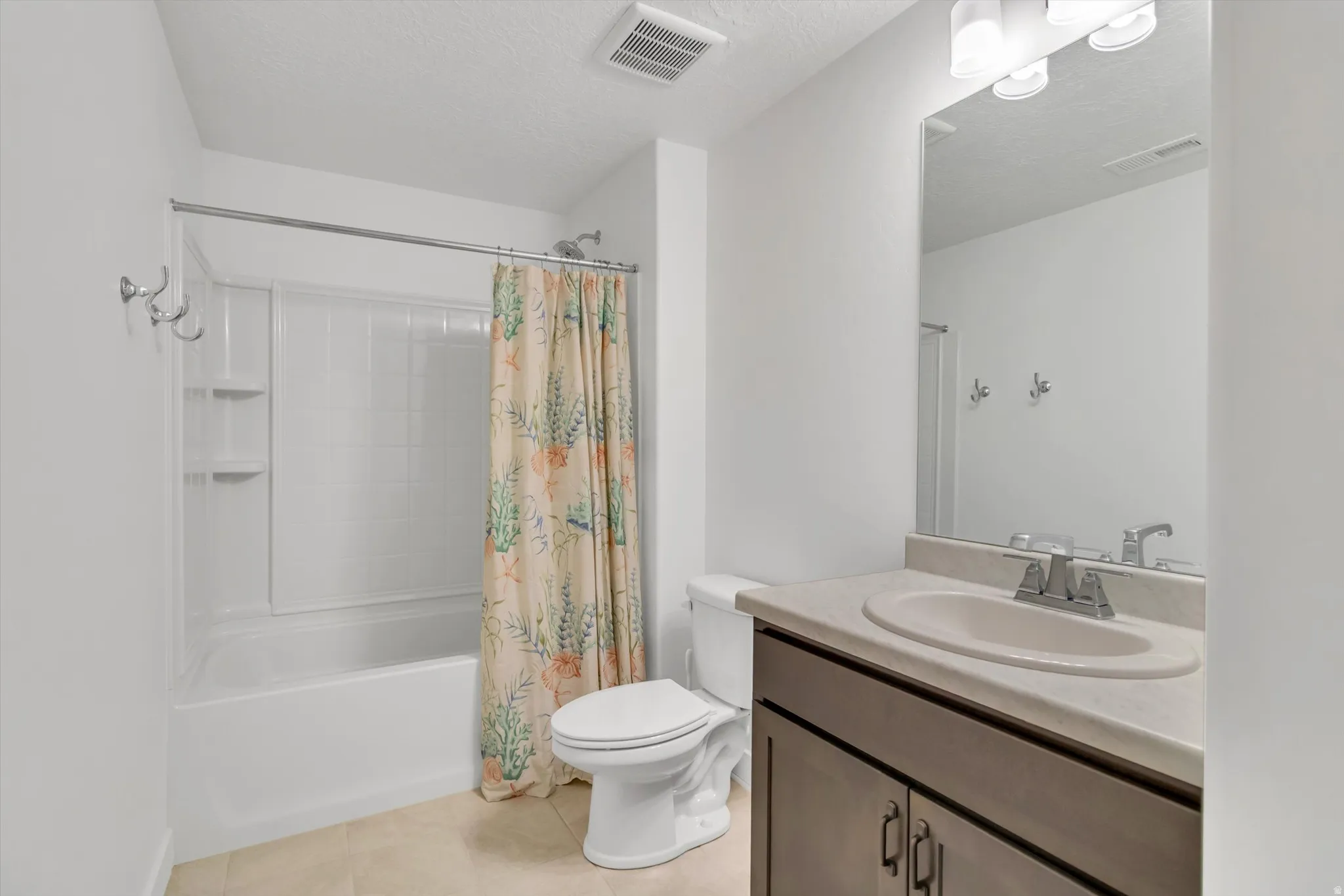 Built-in bathtub with shower, vanity with integrated sink, wall-mounted mirror, and tile flooring