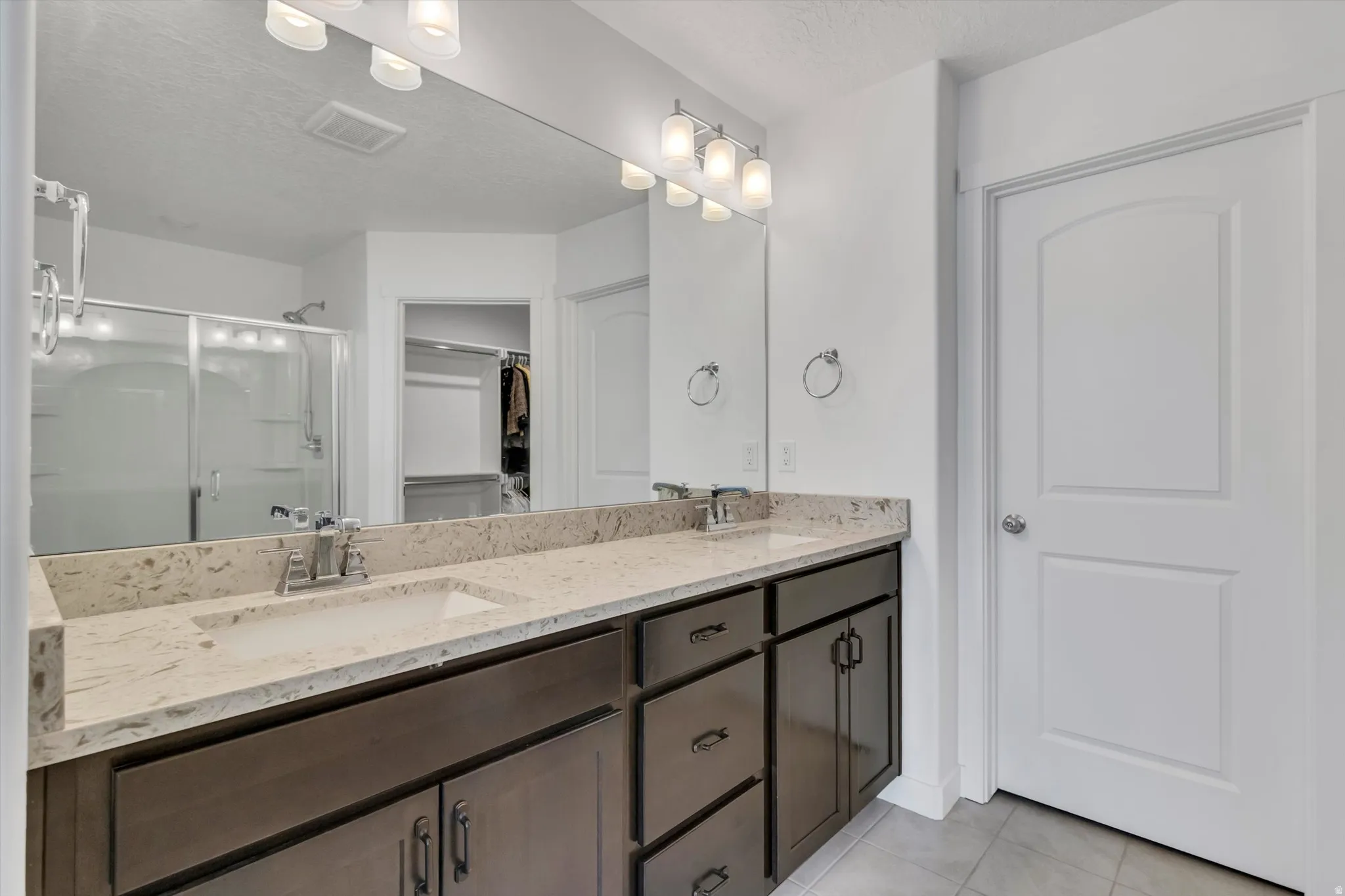 Double vanity with light-toned countertop, dual rectangular undermount sinks, dark wood-finish cabinetry, and chrome fixtures