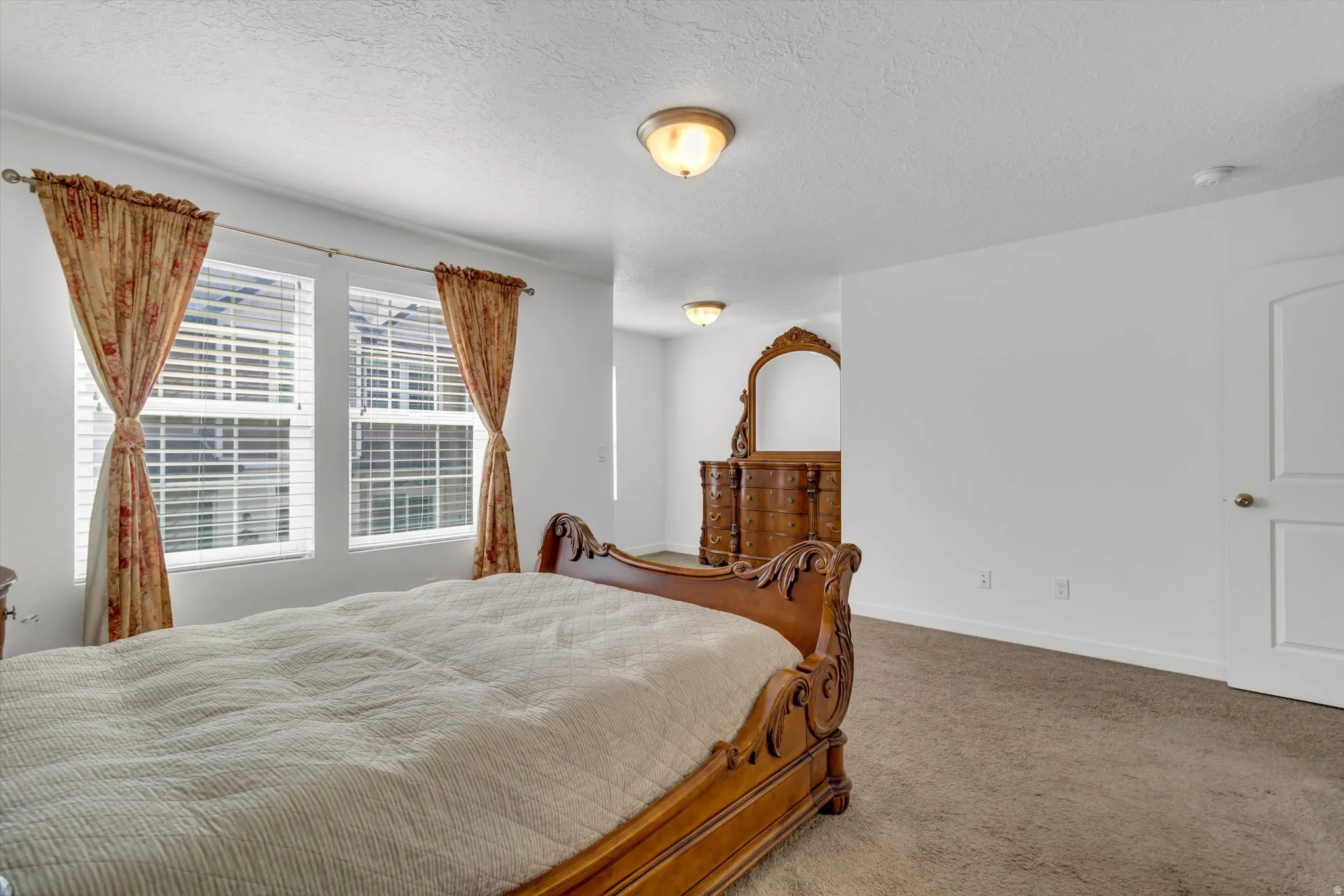 Carpeted flooring, white walls, two windows with blinds, and ceiling-mounted lighting