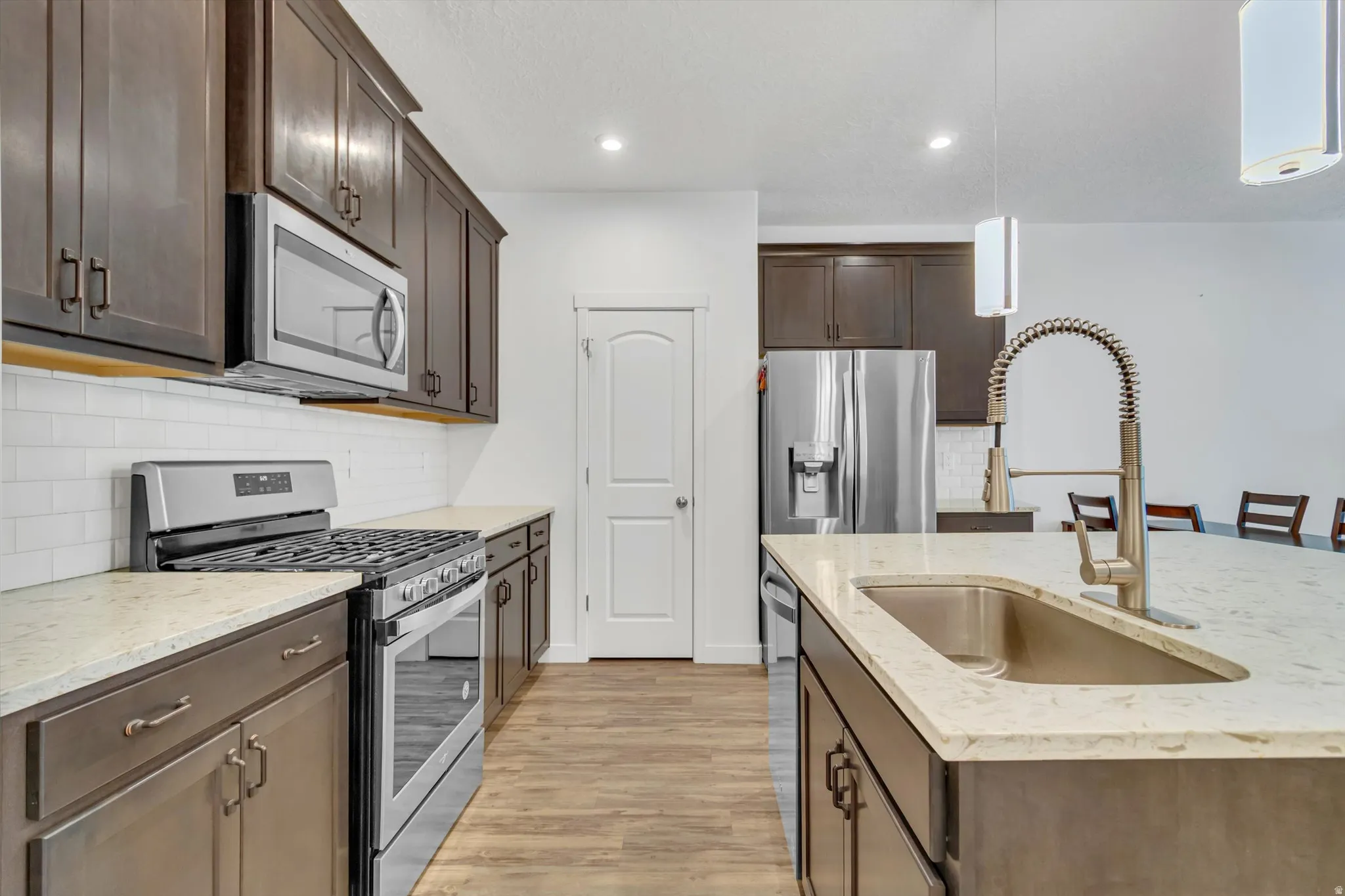 Kitchen featuring dark wood-finish cabinetry, stainless steel appliances, a subway tile backsplash, and light-toned countertops