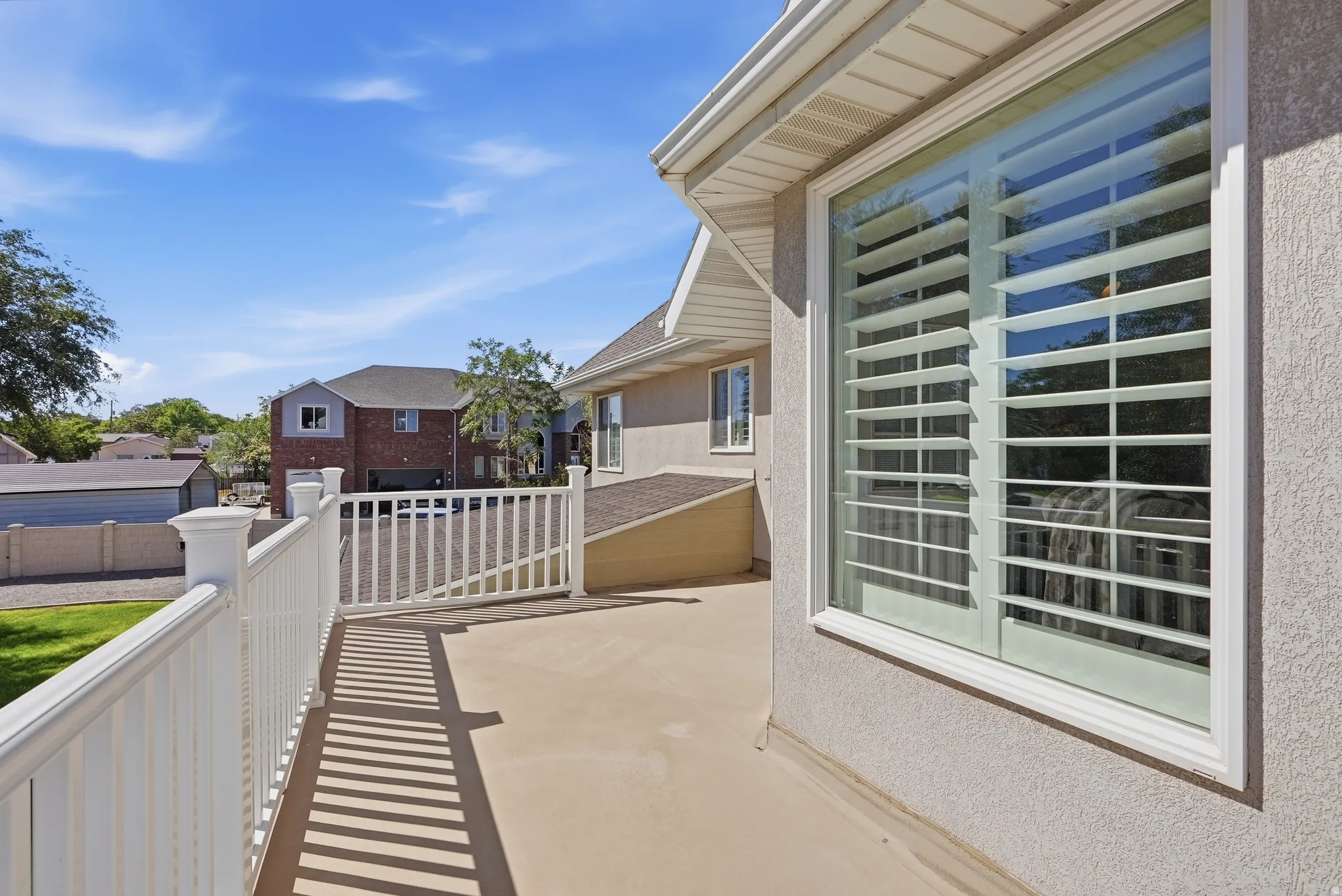Master Suite Outdoor deck with white railing, textured stucco exterior, and a large window with plantation shutters