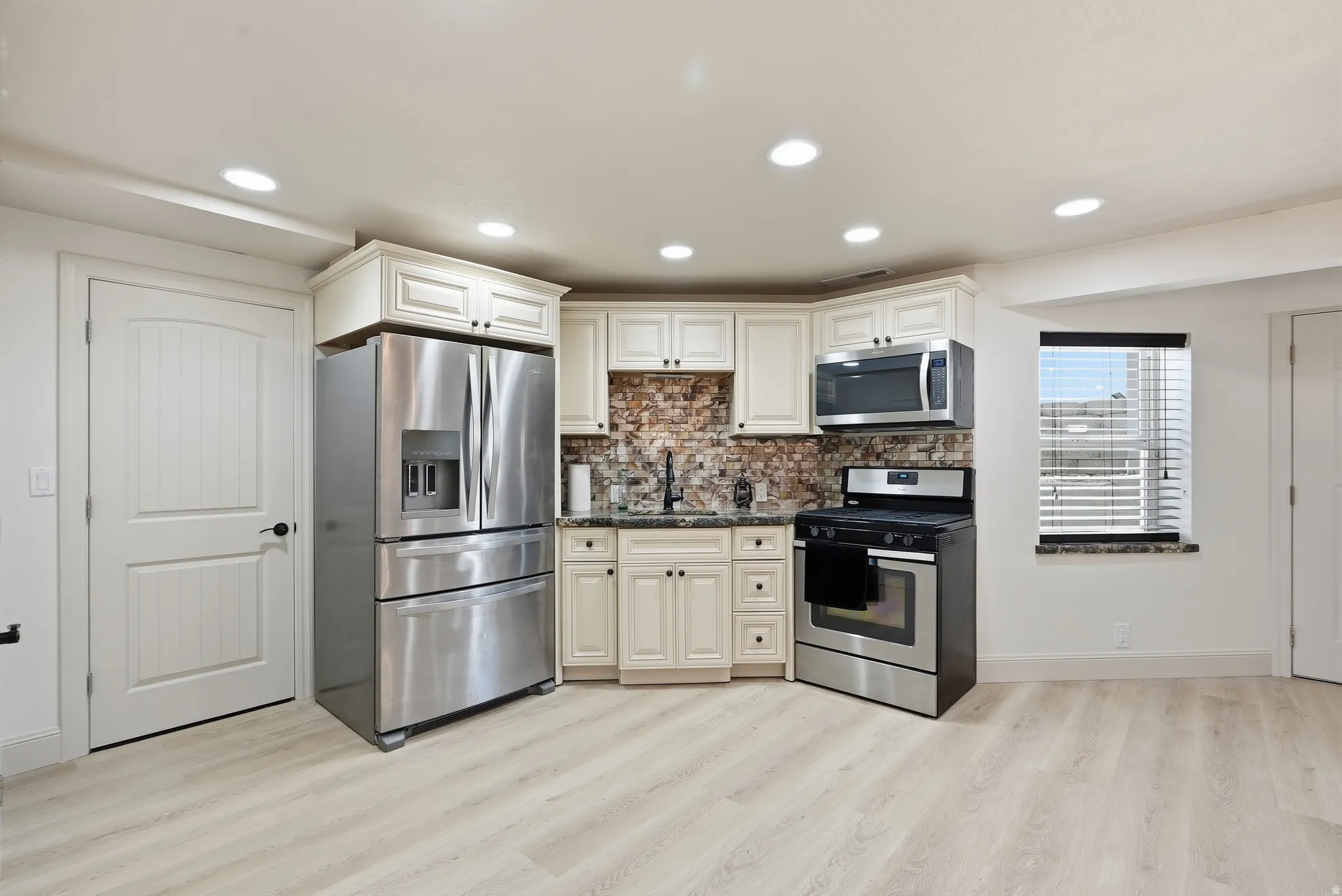 Kitchenette featuring cream cabinetry, stainless steel appliances, mosaic tile backsplash, and light wood-finish flooring