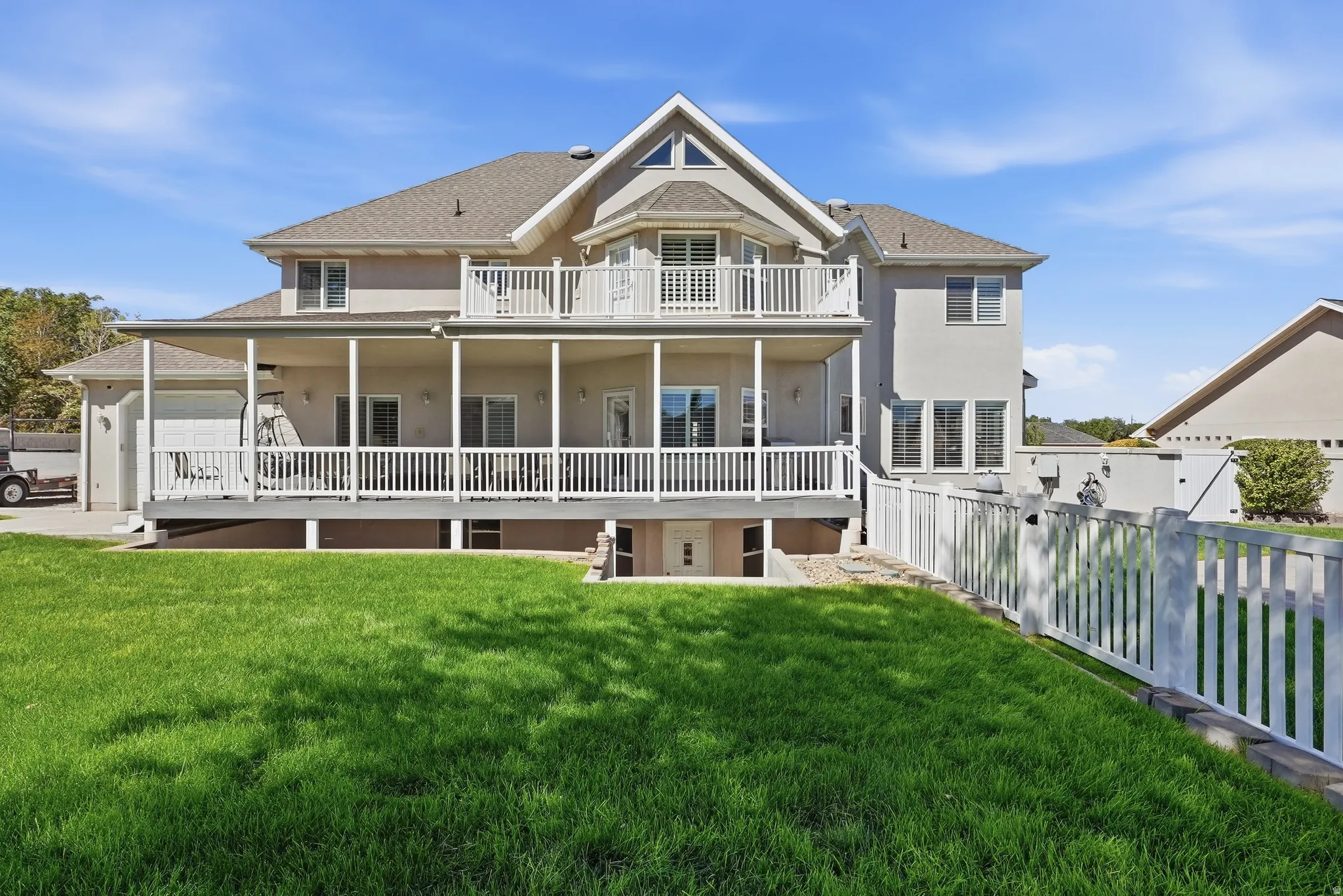 Stucco exterior with multiple balconies, a covered patio, a walk-out basement entrance, and a white picket fence