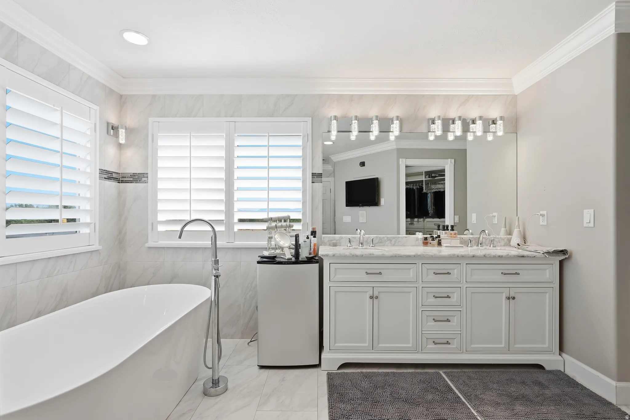 Master Suite: Freestanding soaking tub with floor-mounted faucet, dual windows with plantation shutters, double vanity with dual undermount sinks, and a large wall-mounted mirror
