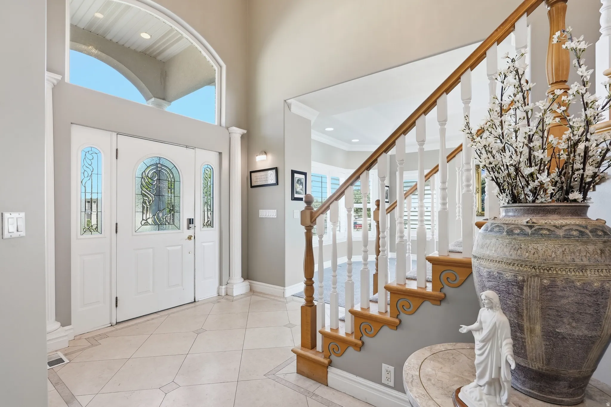 Grand entryway featuring a decorative door with leaded glass, transom window, tile flooring with decorative inlay, and a staircase with wood newel posts and handrail