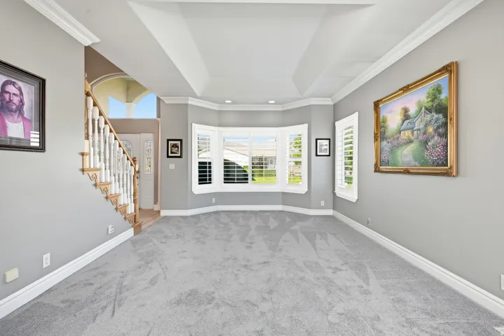 Tray ceiling detail, neutral wall color, bay window with plantation shutters, staircase with wood newel posts and balusters, and crown molding accents