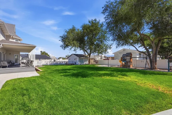 Expansive grassy yard with mature trees, a covered patio with a gray composite deck, and a detached shed