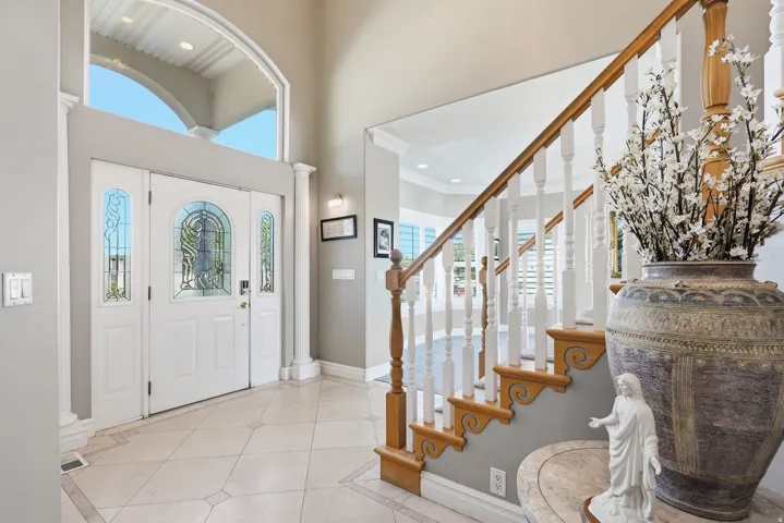 Grand entryway featuring a decorative door with leaded glass, transom window, tile flooring with decorative inlay, and a staircase with wood newel posts and handrail