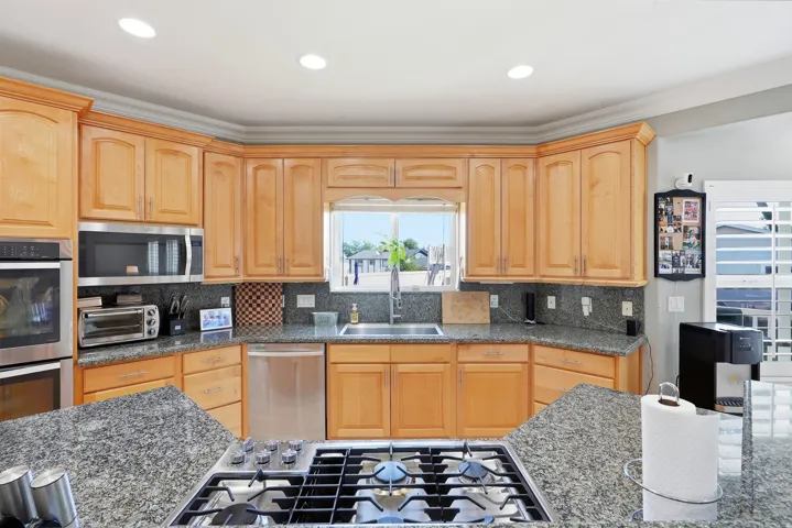 Kitchen featuring wood cabinetry, stainless steel appliances, dark stone countertops, and a built-in cooktop