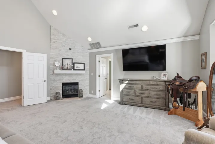 Master Suite: Vaulted ceiling with recessed lighting, stone-clad fireplace with mantel, and light-toned carpeting