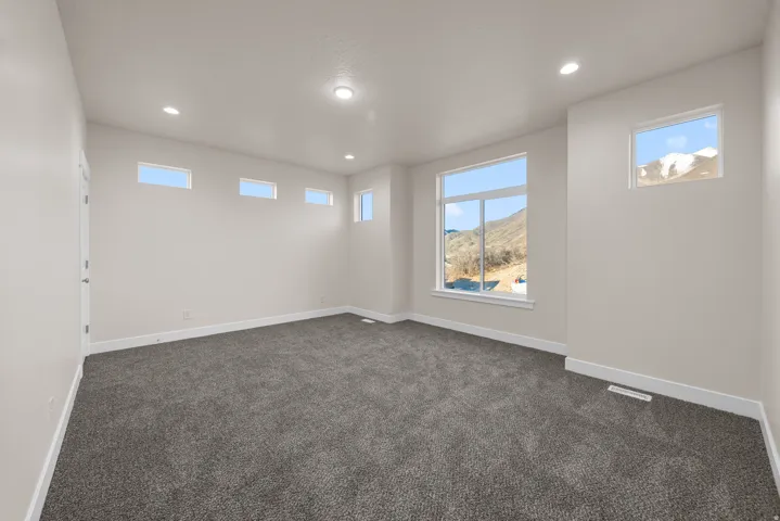 Spacious room featuring neutral carpeting, recessed lighting, and multiple windows providing ambient light