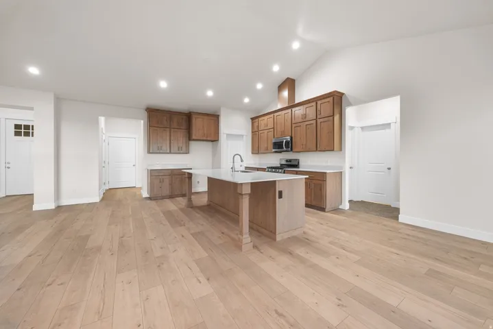 Vaulted ceiling, recessed lighting, wood-finish flooring, kitchen island with sink, and wood cabinetry