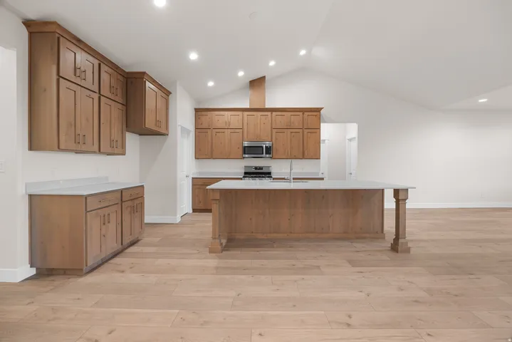 Vaulted ceiling kitchen with wood-finish flooring, light wood cabinetry, white countertops, and a central island