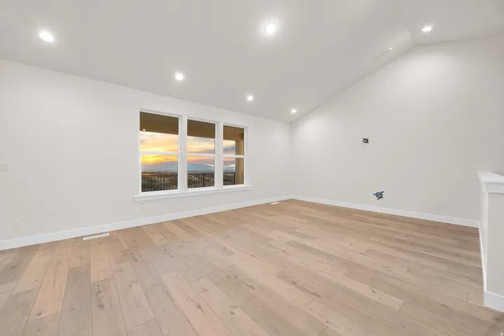 Recessed lighting illuminates the expansive room featuring wood-finish flooring, a vaulted ceiling, and multiple windows