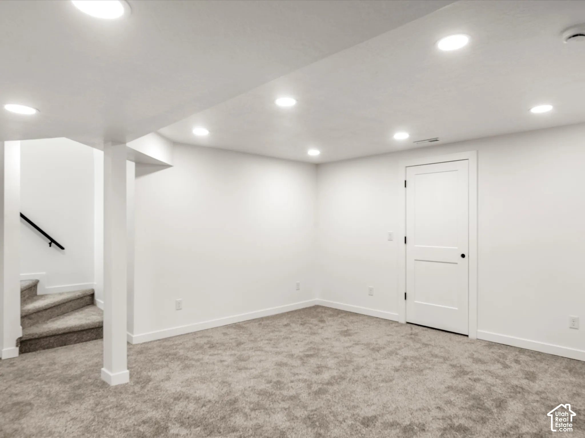 Basement family room. Recessed lighting, light gray carpeting, white walls, white trim, and a white interior door with black hardware