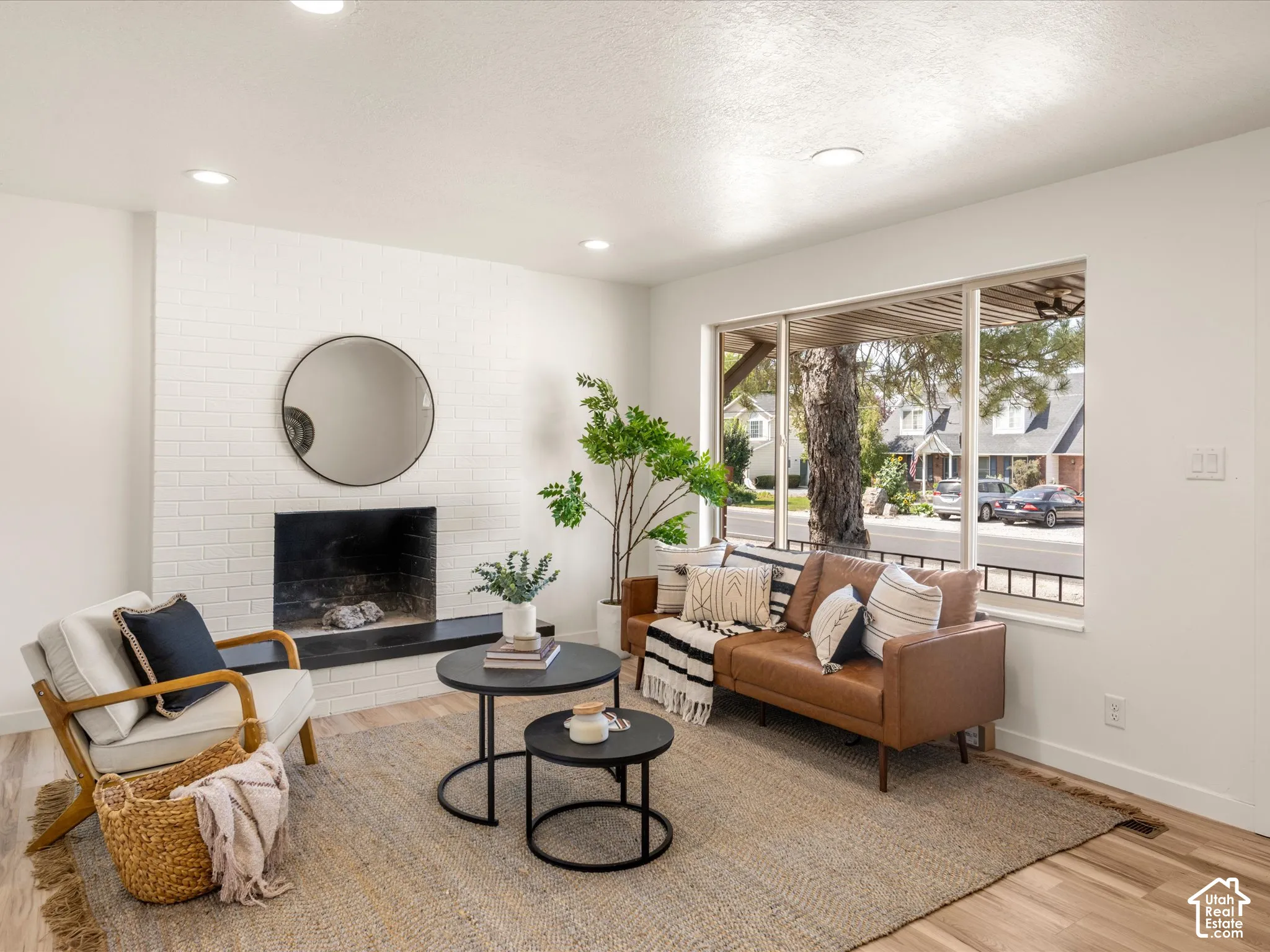 Living area featuring a white brick fireplace with a dark hearth, recessed lighting, wood-finish flooring, and a large window