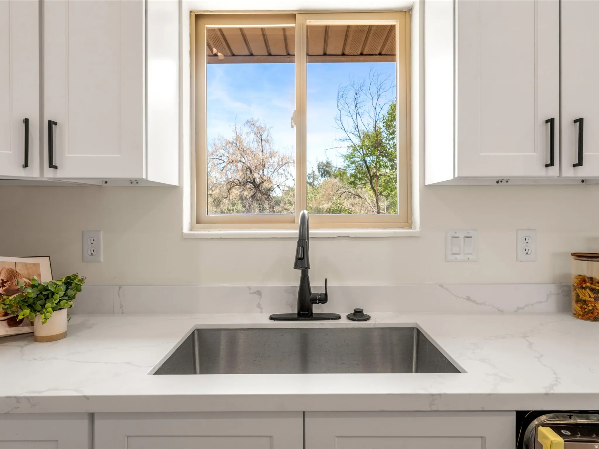 White shaker cabinetry with matte black hardware, undermount stainless steel sink, solid surface countertops, and a single-handle matte black faucet