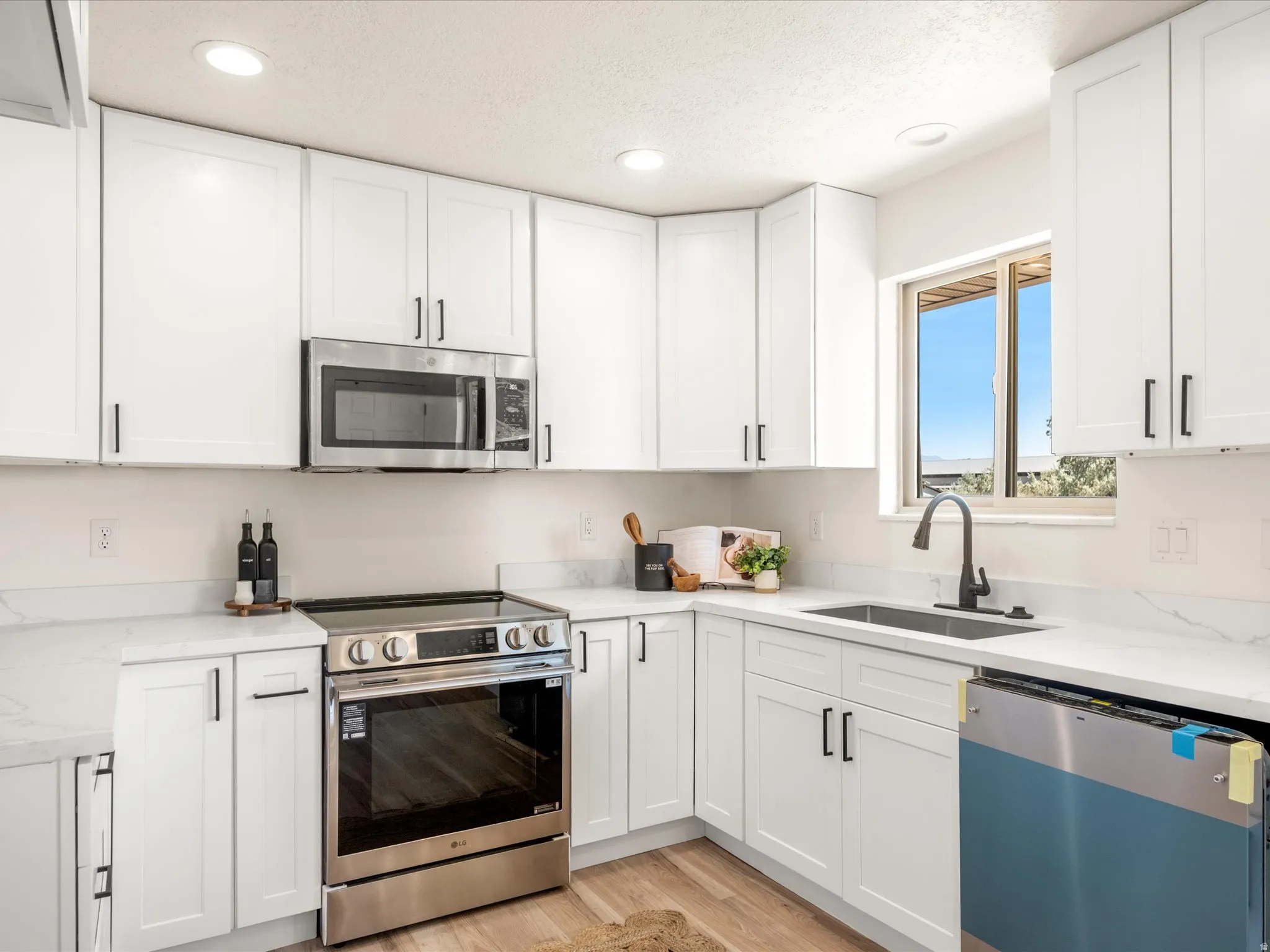 White shaker cabinetry, stainless steel appliances, undermount sink with a matte black faucet, recessed lighting, and light-toned wood-finish flooring
