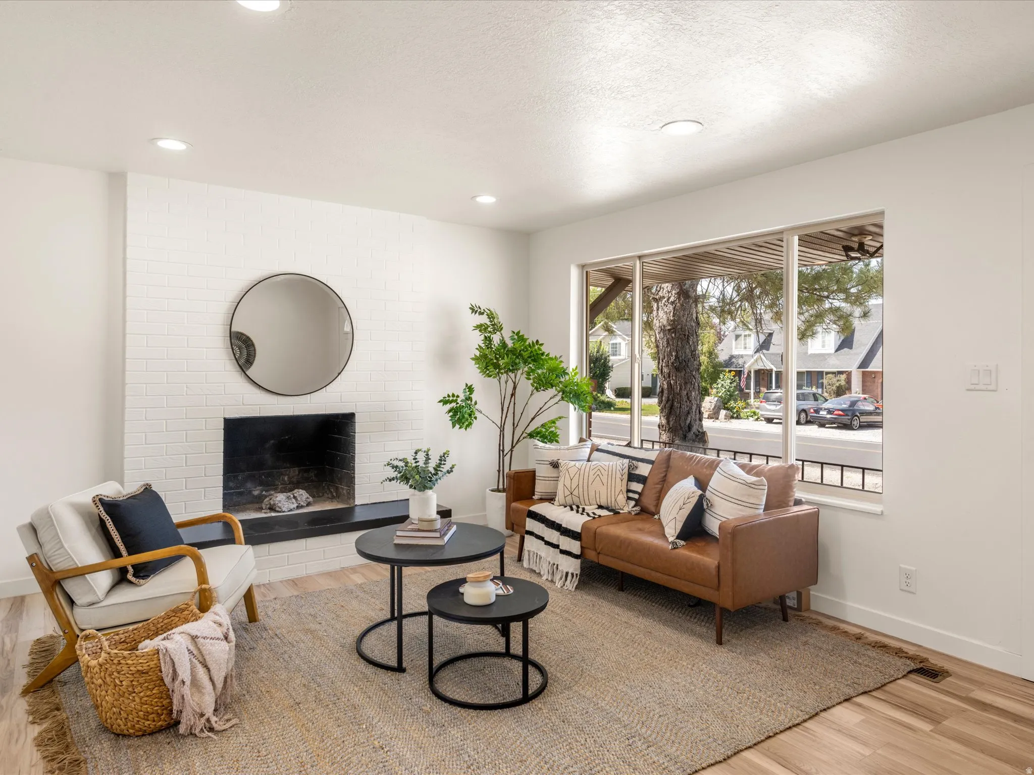 Living area featuring a white brick fireplace with a dark hearth, recessed lighting, wood-finish flooring, and a large window