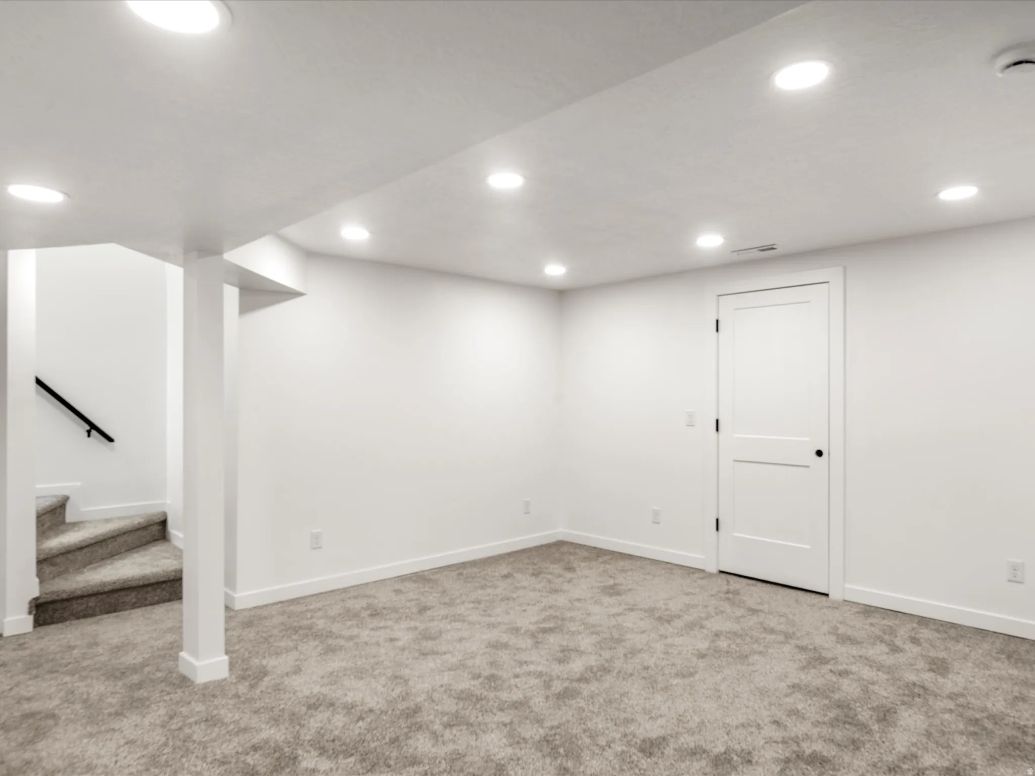 Basement family room. Recessed lighting, light gray carpeting, white walls, white trim, and a white interior door with black hardware