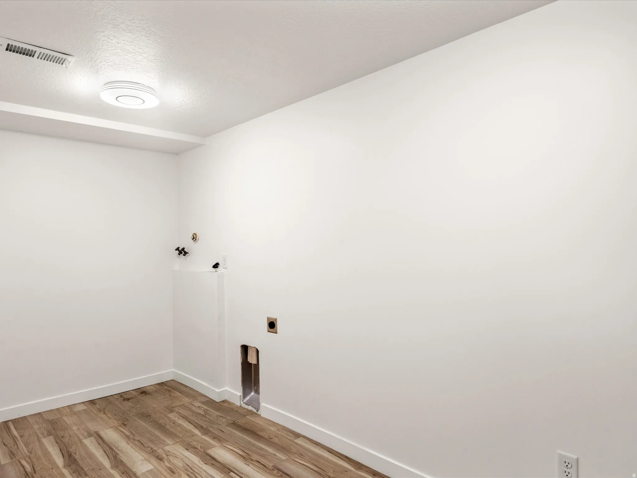 Laundry space with wood-finish flooring, white walls, and a flush-mount ceiling light