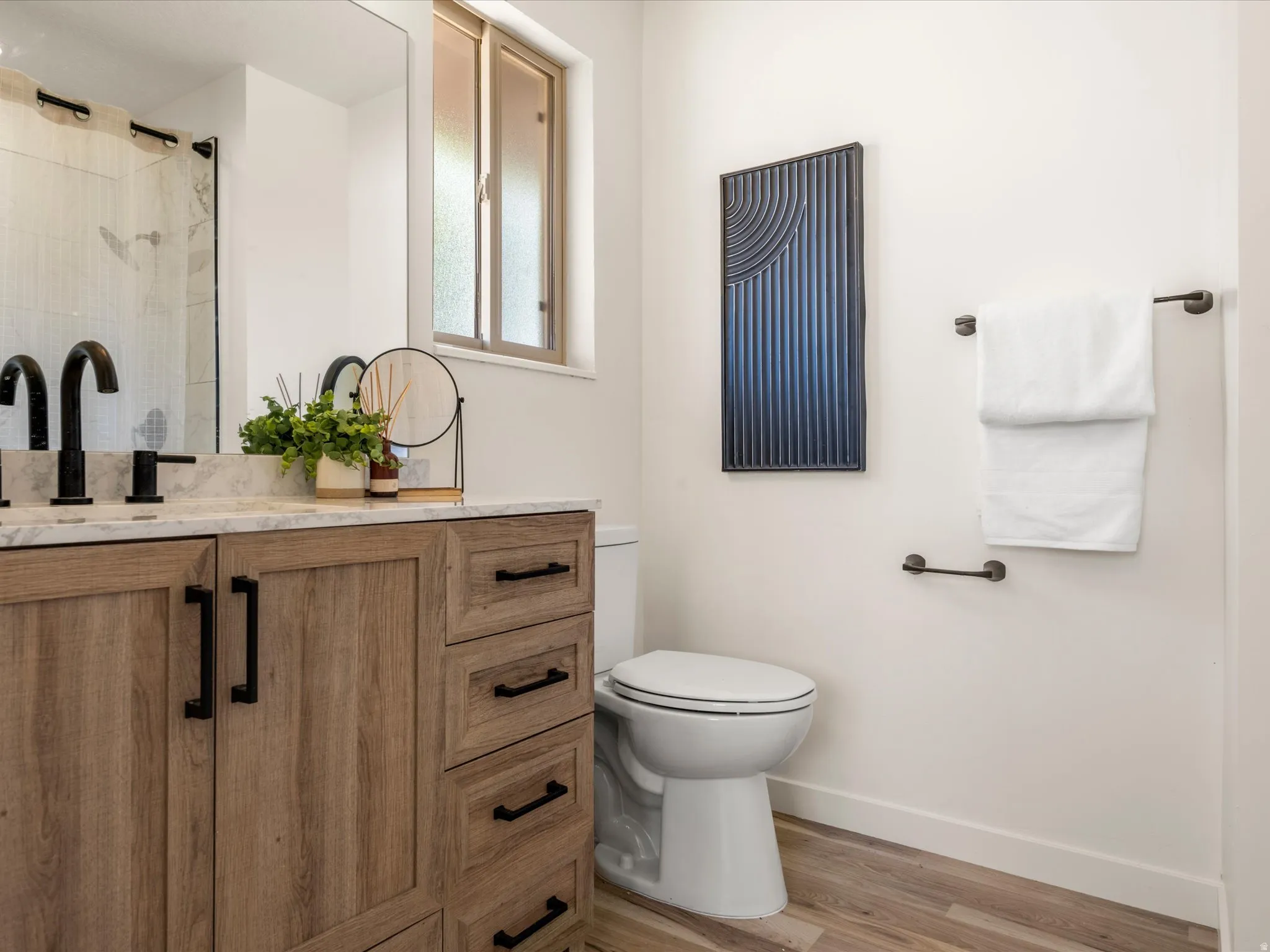 Primary Bathroom with Shower and walk in closet. Dual sink vanity with a stone countertop, matte black fixtures, wood-finish flooring, and a shower with a glass enclosure