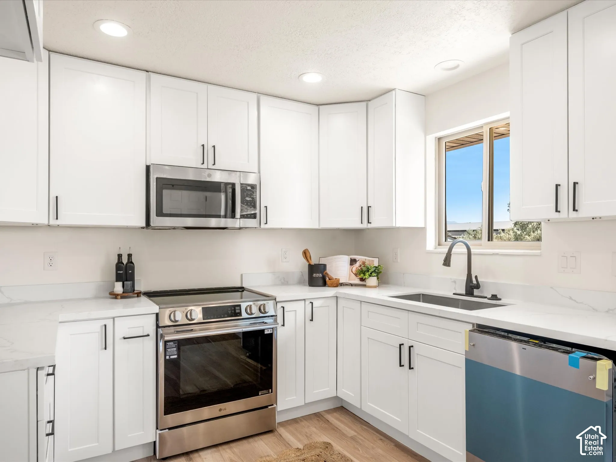 White shaker cabinetry, stainless steel appliances, undermount sink with a matte black faucet, recessed lighting, and light-toned wood-finish flooring