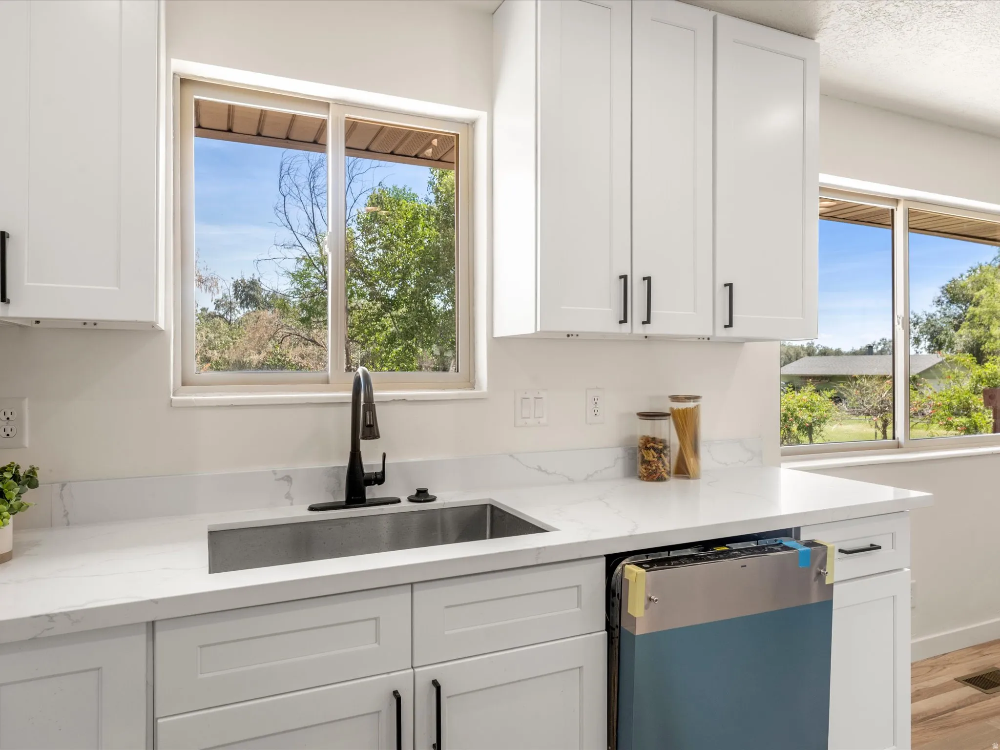 White shaker-style cabinetry with matte black hardware, stainless steel undermount sink, black gooseneck faucet, and light-colored countertops with veining