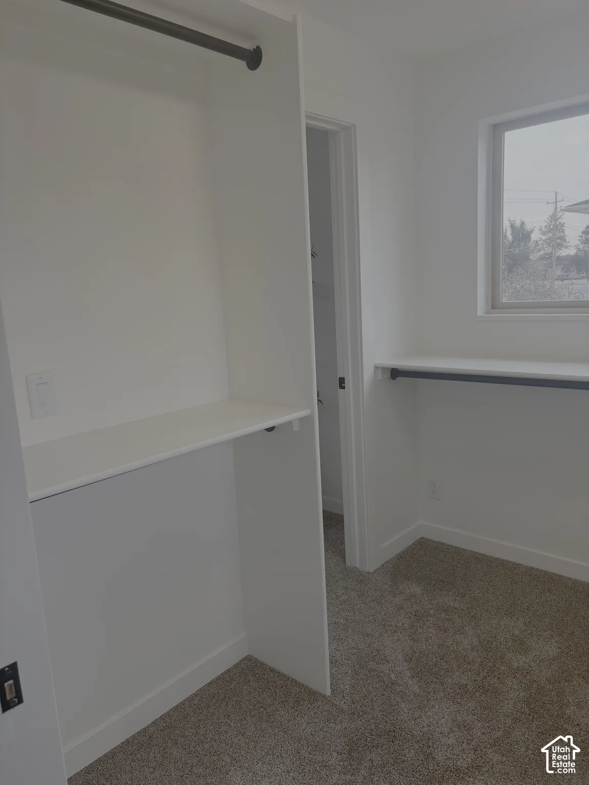 Walk-in closet featuring white built-in shelving, dark-finish hanging rods, and textured carpeting