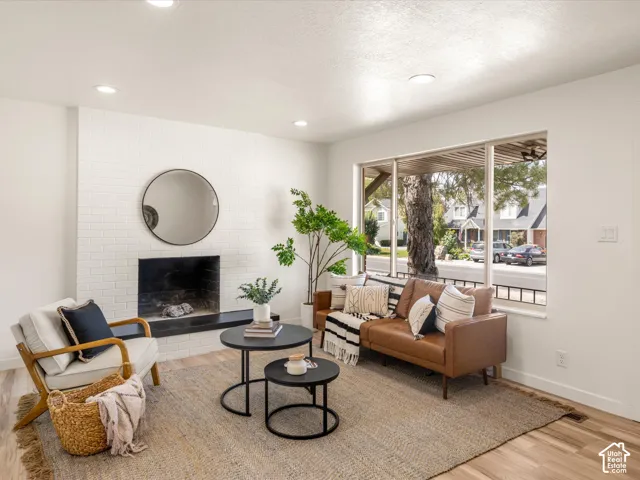 Living area featuring a white brick fireplace with a dark hearth, recessed lighting, wood-finish flooring, and a large window