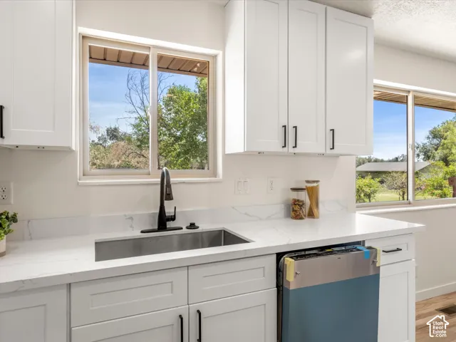 White shaker-style cabinetry with matte black hardware, stainless steel undermount sink, black gooseneck faucet, and light-colored countertops with veining