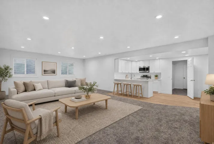 Open-concept living space featuring recessed lighting, a modern kitchen with white cabinetry, stainless steel appliances, and a breakfast bar, wood-finish flooring, and two visible windows
