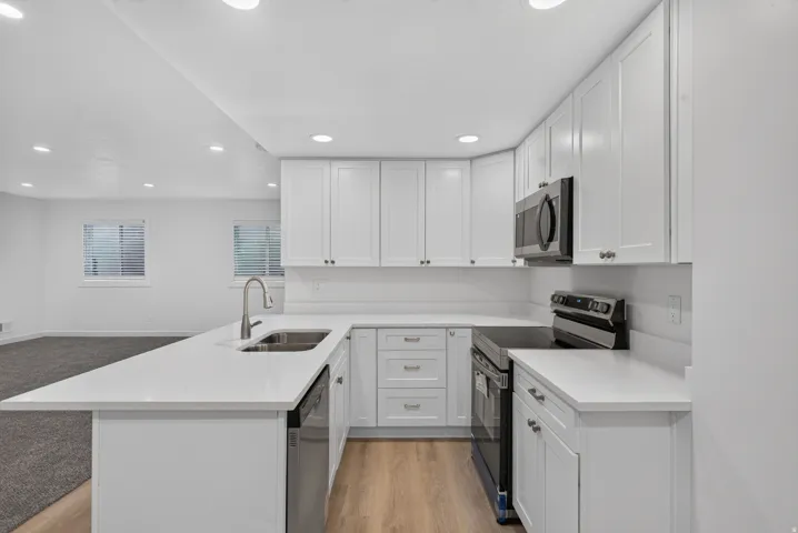 White shaker cabinetry, stainless steel appliances, recessed lighting, wood-finish flooring, and light-toned countertops