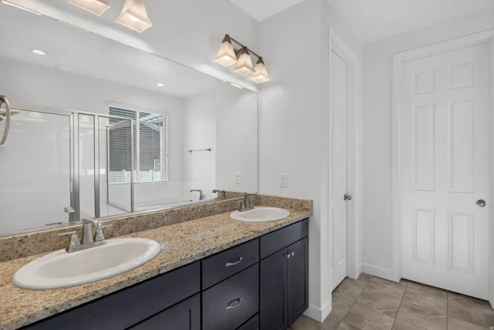 Dual vanity with granite countertop, dark wood-finish cabinetry, and brushed nickel fixtures