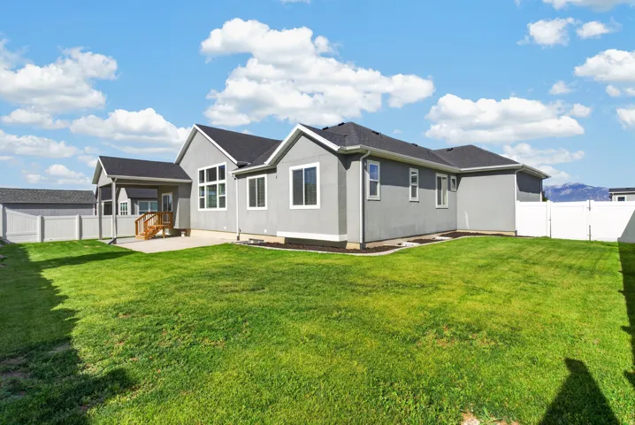 Expansive backyard featuring a concrete patio, covered porch with wood deck, and partial vinyl fencing