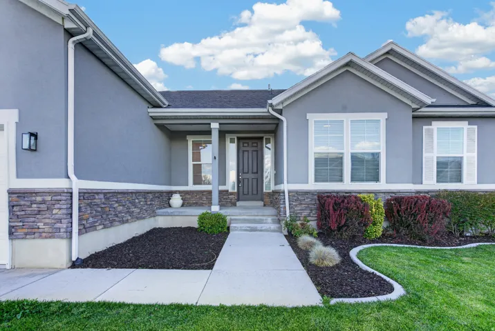 Exterior featuring stucco siding, stone facade accents, covered entry, front door with sidelight, and well-defined landscaping